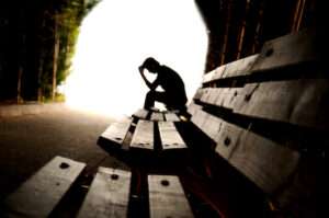 On the right handside there are three benches one after the other in a line into the distance. They are within a tunnel and you can see the light at the end. On the last bench is the silhouette of someone who is sat there leaning forwards with their head in their hands.