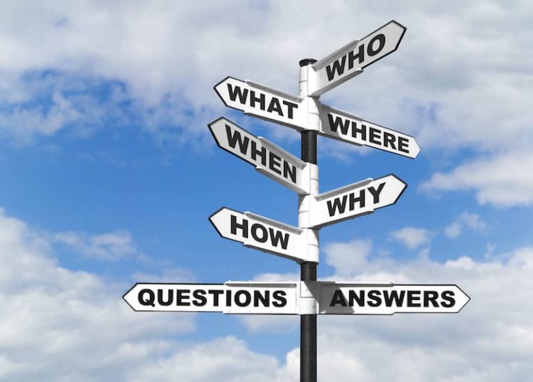 Photo of a black signpost pole. On it there are 8 signs with black writing on white backgrounds all pointing in different directions. From top to bottom they ready Who, What, Where, When, Why, How, Questions, Answers. the background is a bright sky with some white clouds