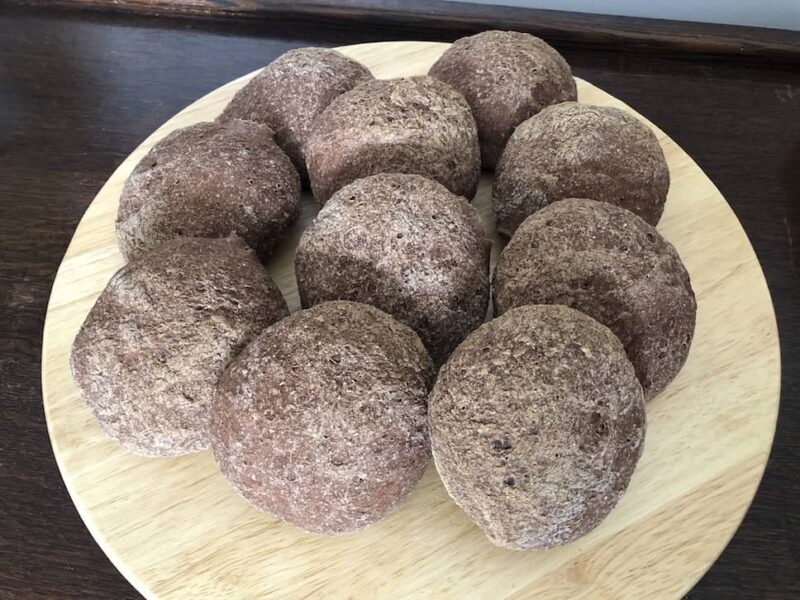Photo of ten home made gluten free Teff rolls on a wooden circular board. They are porpped up against each other and you can see how full they are.