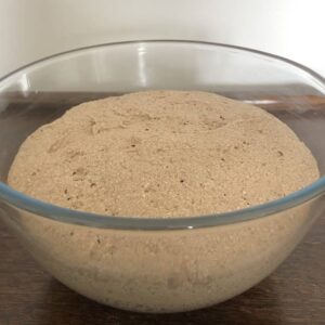 Photo of the Teff roll dough in a large glass fully risen to double its size.