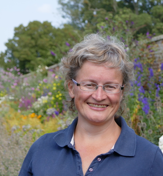 An image of Rachael Kennard-Wall smiling she is stood outside with the background of a walled garden and country garden flowers.