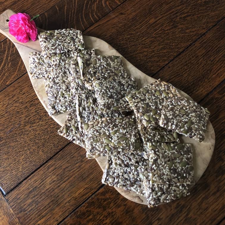 Wooden board loaded with a batch of gluten free seeded crackers ready to eat.