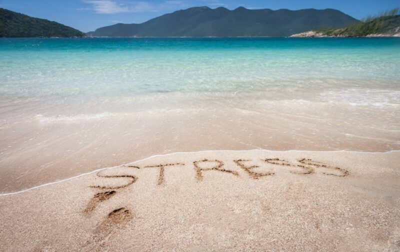 This is the header for a blog describing how stress and other trapped emotions can be the cause to chronic pain remaining. This image is of a beautiful tranquil blue sea with nothing to see but the water stretching out until you reach a hilly coastline or island in the distance. The sky is blue and in the fore ground in the sand you can see two foot prints and the word stress which someone has drawn in the sand. The sea is about to wash over it and erase the stress. This is a pictoral illustration of how stress can be removed and pain can resolve.