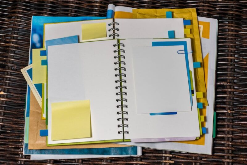 An image of piled up notebooks with post it notes to illustrate procrastinate and how we think we just need to get more organised.