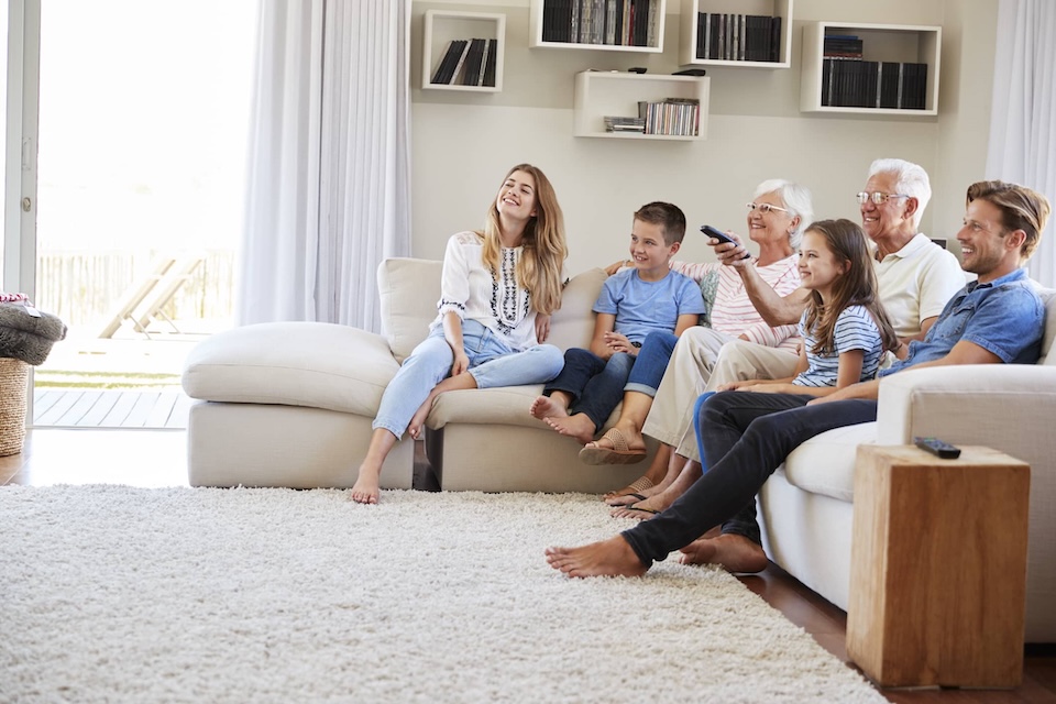 a family sat around on a big cream sofa with a fluffy cream rug in front of them there are three generations sat around looking at a TV that you can't see in the image smiling and looking like they are enjoying it. What better way to strengthen your immune system.